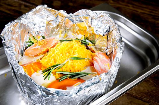 Meat with vegetables in foil on Protvino. Wooden background.