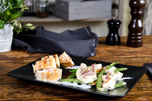 Stuffed turkey breast on the black plate snd wooden background. Chicken roulade - Stock image