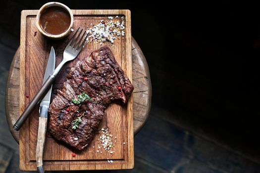 Beef steak. Piece of Grilled BBQ beef marinated in spices and herbs on a rustic wooden board over rough wooden desk with a copy space. Top view. Stock Image