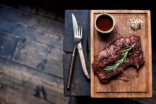 Beefsteak. Piece of grilled BBQ beef marinated in spices and herbs on rustic wooden board over rough wooden desk with copy space. Top view.