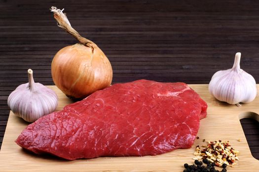 Raw Beef Roast with Fresh Herbs on a dark wooden table.