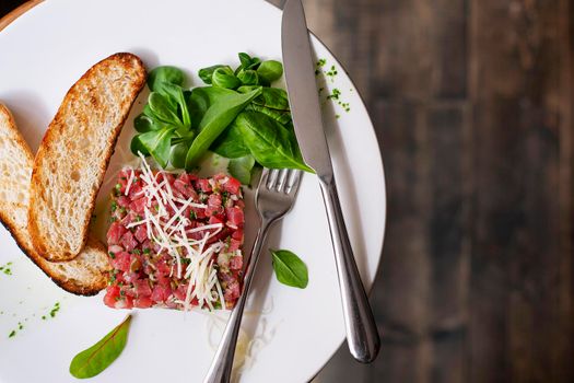 Tartare of beef with spinach on a white plate. Isolated on black.