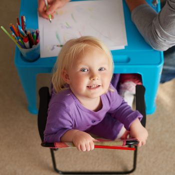 Portrait of an adorable little girl colouring in at her own small table at home.