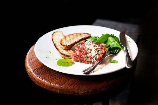 Tartare of beef with spinach on a white plate. Isolated on black or dark wooden background.