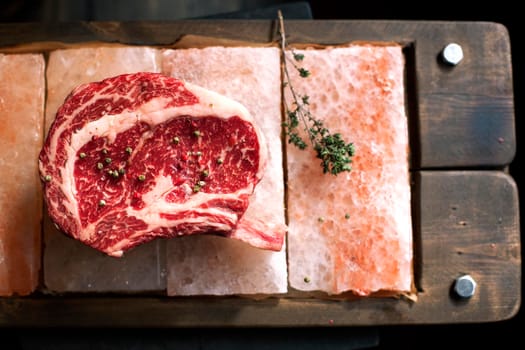 Bone In Rib Eye row Steak on pieces of salt on a wooden board. Stock image