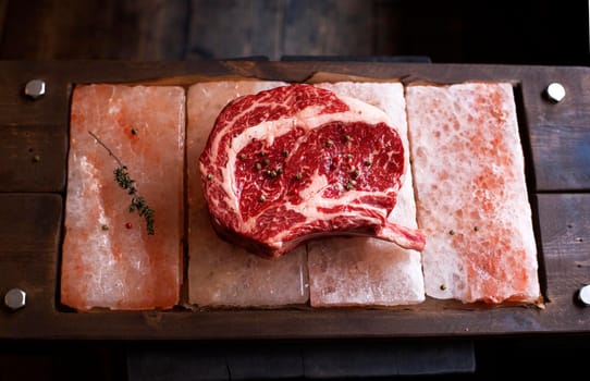 Bone In Rib Eye row Steak on pieces of salt on a wooden board. Stock image