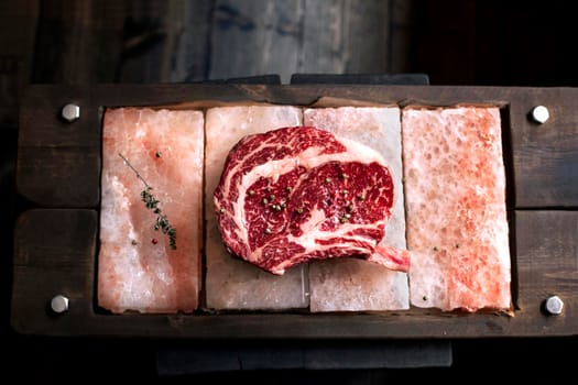 Bone In Rib Eye row Steak on pieces of salt on a wooden board. Stock image