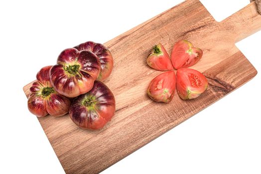 Tiger tomato on a cutting board with basil leaves on wooden background. Copy space. Fresh tomato wased for cooking. Tomato with droplets of water