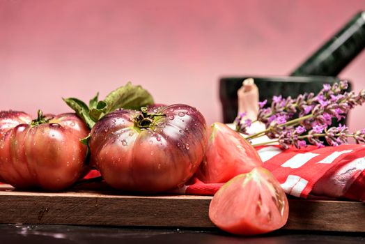 Tiger tomato on a cutting board with basil leaves on wooden background. Copy space. Fresh tomato wased for cooking. Tomato with droplets of water