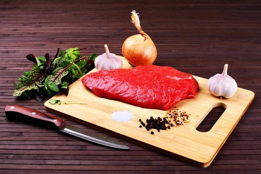 Raw Beef Roast with Fresh Herbs on a dark wooden table.