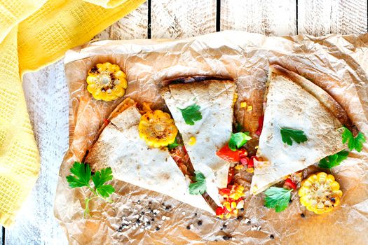 Mexican Quesadilla wrap with vegetables, corn, sweet pepper and sauces on the parchment and table. horizontal view.