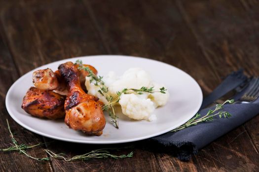 Baked chicken drumsticks with cauliflower served on a wooden table. Rustic style