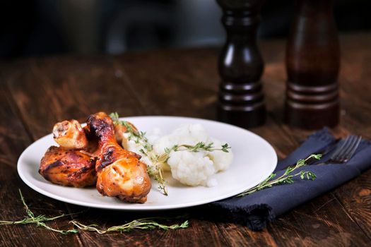 Baked chicken drumsticks with cauliflower served on a wooden table. Rustic style