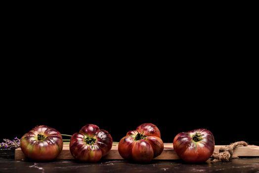 Tiger tomato on a cutting board with basil leaves on wooden background. Copy space. Fresh tomato wased for cooking. Tomato with droplets of water