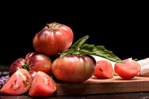 Tiger tomato on a cutting board with basil leaves on wooden background. Copy space. Fresh tomato wased for cooking. Tomato with droplets of water