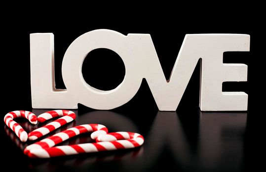 large letters LOVE and Valentine Heart made from Christmas candies isolated on black background