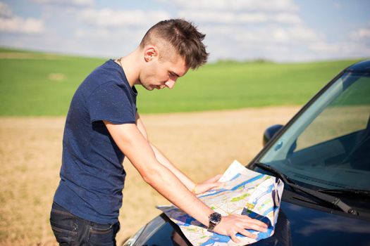 Photo of a traveler parked his car by the side of a road, lost and reading the map. Focus on the map and male.