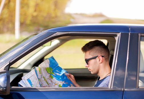 Photo of a traveler parked his car by the side of a road, lost and reading the map. Focus on the map and male.