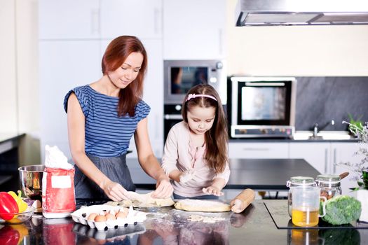 Mother with little daughter cooking in the kitchen at home. Girl Assisting In Preparing Food - Stock image