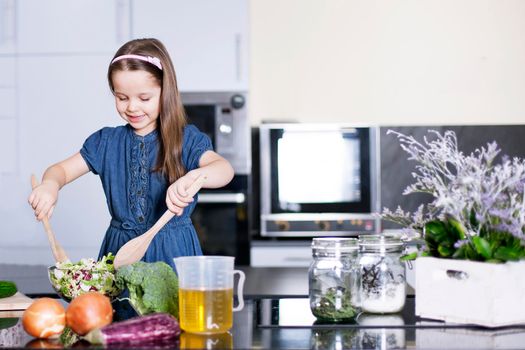 little daughter cooking in the kitchen at home. Girl Assisting In Preparing Food - Stock image