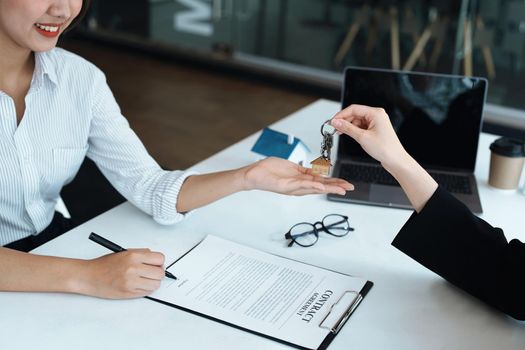 Accountant, businessman, real estate agent, Asian business woman handing keys to customers along with house after customers to sign.