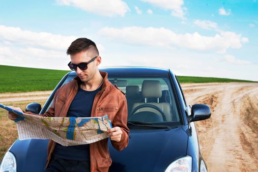 Photo of a traveler parked his car by the side of a road, lost and reading the map. Focus on the map and male.