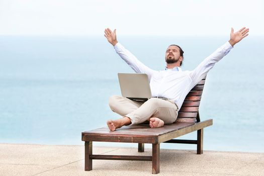 Young businessman on the beach resting on his deck chair using his tablet. luky winner.