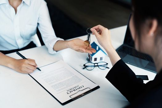 Accountant, businessman, real estate agent, Asian business woman handing keys to customers along with house after customers to sign.