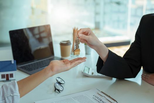 Accountant, businessman, real estate agent, Asian business woman handing keys to customers along with house after customers to sign.