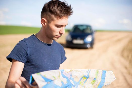 Photo of a traveler parked his car by the side of a road, lost and reading the map. Focus on the map and male.