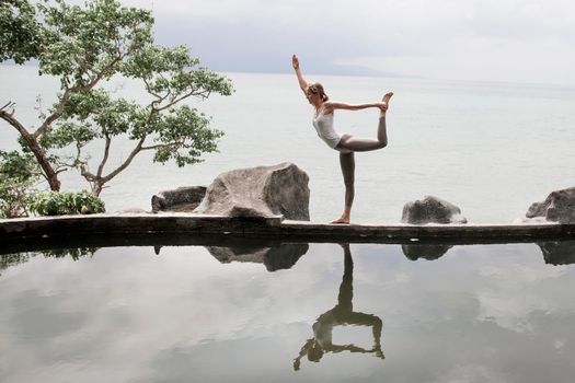 The silhouette of a beautiful young woman practicing yoga in front of the lake at sunrise.