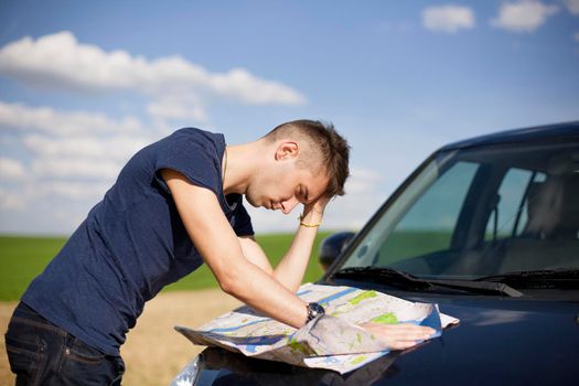 Photo of a traveler parked his car by the side of a road, lost and reading the map. Focus on the map and male.