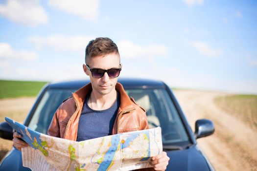 A tourist man next to the car looks at the map of the area for further travel.