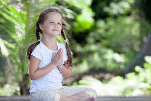 Child doing exercise on platform outdoors. Healthy ocean lifestyle. Yoga girl