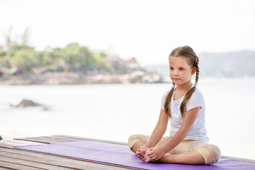 Child doing exercise on platform outdoors. Healthy ocean lifestyle. Yoga girl