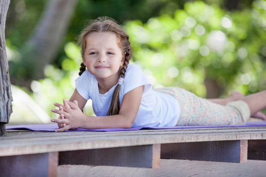 Child doing exercise on platform outdoors. Healthy ocean lifestyle. Yoga girl