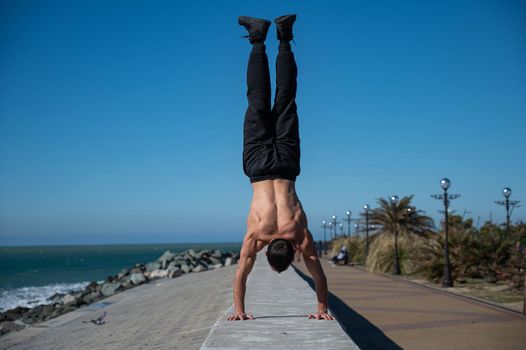 Shirtless man doing a handstand on the seashore