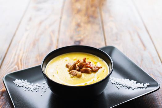 Pumpkin vegetable cream soup on black bowl with pork or chicken meat. Wooden background