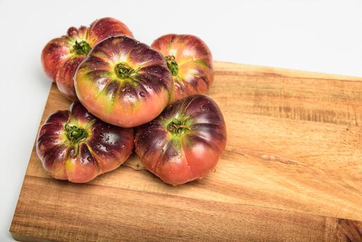 Tiger tomato on a cutting board with basil leaves on wooden background. Copy space. Fresh tomato wased for cooking. Tomato with droplets of water