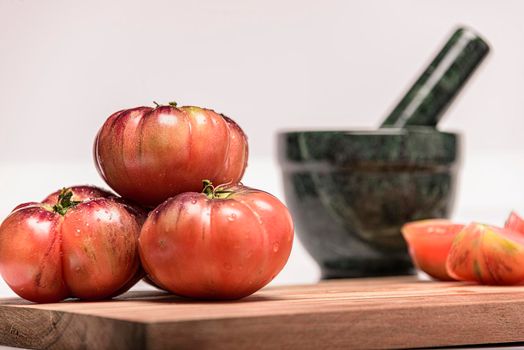 Tiger tomato on a cutting board with basil leaves on wooden background. Copy space. Fresh tomato wased for cooking. Tomato with droplets of water