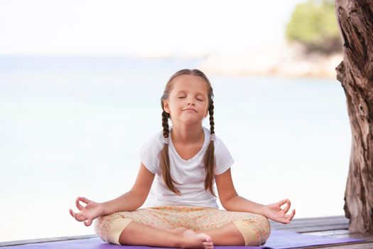 Child doing exercise on platform outdoors. Healthy ocean lifestyle. Yoga girl