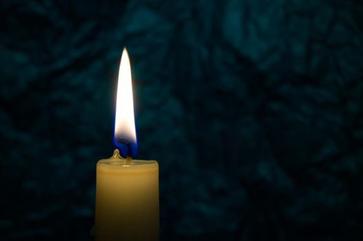 Single yellow wax candle burning alone in the dark background. Conceptual image symbolize peace, love, hope or patience with free copy space