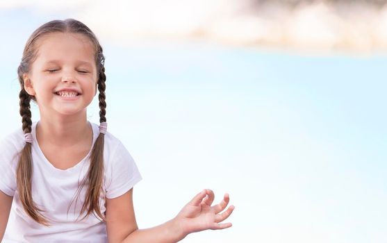 Child doing exercise on platform outdoors. Healthy ocean lifestyle. Yoga girl