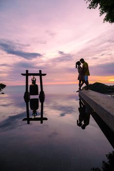 a young couple of men and women at a swimming pool during a vacation on a tropical island. man and woman in infinity pool during sunset. luxury vacation in Thailand pool of a luxury pool villa