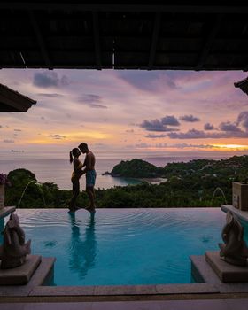 a young couple of men and women at a swimming pool during a vacation on a tropical island. man and woman in infinity pool during sunset. luxury vacation in Thailand pool of a luxury pool villa