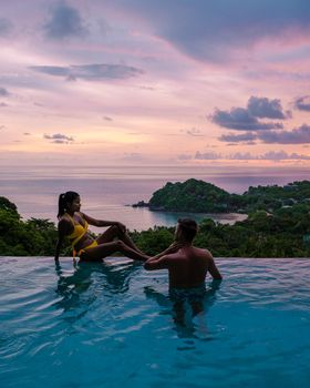 a young couple of men and women at a swimming pool during a vacation on a tropical island. man and woman in infinity pool during sunset. luxury vacation in Thailand pool of a luxury pool villa