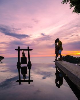 a young couple of men and women at a swimming pool during a vacation on a tropical island. man and woman in infinity pool during sunset. luxury vacation in Thailand pool of a luxury pool villa