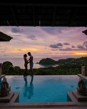 a young couple of men and women at a swimming pool during a vacation on a tropical island. man and woman in infinity pool during sunset. luxury vacation in Thailand pool of a luxury pool villa