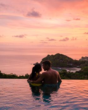 a young couple of men and women at a swimming pool during a vacation on a tropical island. man and woman in infinity pool during sunset. luxury vacation in Thailand pool of a luxury pool villa