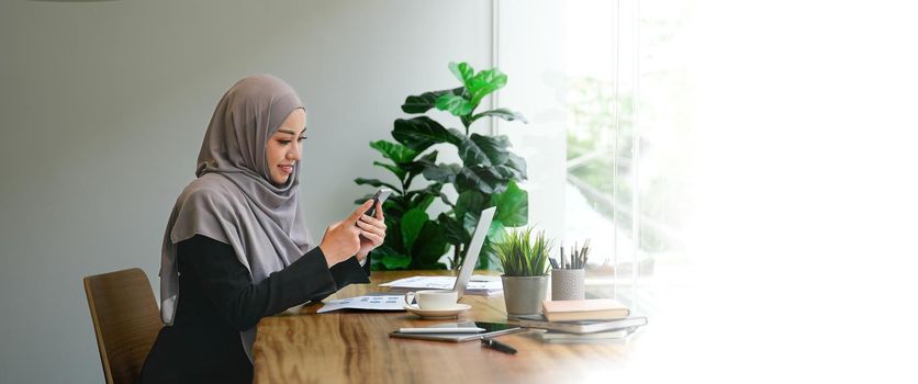 Muslim asian woman using mobile phone and laptop computer at modern office
